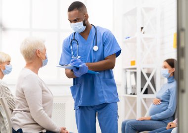 Erkek hemşire, Kıdemli Hasta Kadın 'la Doktor randevusundan önceki 19 semptomu konuşuyor. Hastanede kuyrukta oturuyor, maske takıyor. Coronavirus, Kapalı Tıbbi Tedavi Konsepti