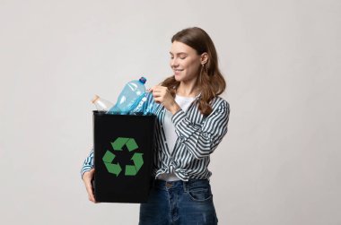 Atık Geri Dönüşüm Konsepti. Elinde plastik şişeler ve yeşil geri dönüşüm tabelasıyla gülümseyen genç bir kadın, Milenyum Çevre dostu kadın stüdyoda Gri Arkaplan 'ın başında duruyor.