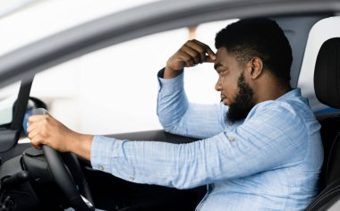 Depresyonda olan Afrikalı adam yeni pahalı bir arabanın sürücü koltuğunda oturuyor, araba galerisinde para sorunları düşünüyor.