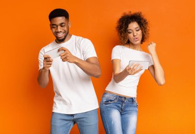 Genç Afro-Amerikan erkek ve birlikte oynama ve video oyunları akıllı telefonlar, turuncu arka plan üzerinde yarışan kadın heyecanlı