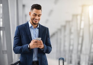 Mobil İletişim. Havalimanı Terminalinde beklerken akıllı telefon kullanan yakışıklı Middel İşadamı, Arkadaşlarıyla Neşeli Arap Mesajlaşan ya da İnternet Tarayıcı, Uzay Kopyalama