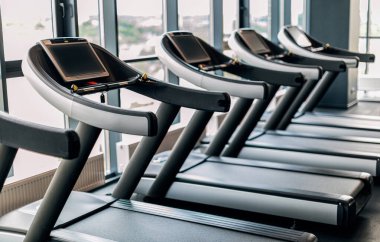 Sport Equipment. Modern Treadmills With Control Panels Standing In A Row At Gym Interior, Closeup Shot Of Training Tools For Running Placed Near Panoramic Windows In Fitness Club Without Visitors