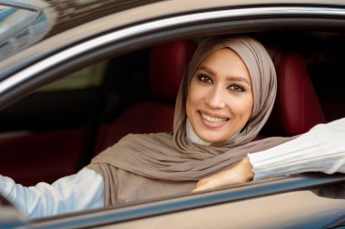 Kiralama ve Test Sürüşü Konsepti. Yeni lüks bir araba kullanan, kameraya bakan tesettürlü müslüman kadının portresi. Ön koltukta oturan ve poz veren başörtülü pozitif Orta Doğulu kadın.