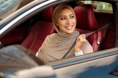 Güvenlik kavramı. Gülümseyen Orta Doğu 'lu kadın oruç tutan emniyet kemeri takıyor, şehirde araba sürüyor. Lüks otomobilinde oturan genç bayan, güvenli sürüş kurallarını takip ediyor, yolculuğa hazır.
