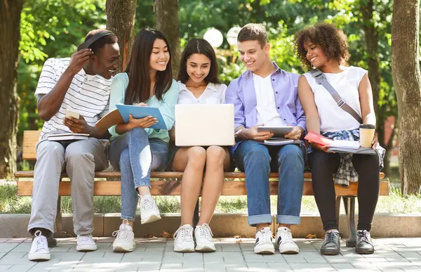 Öğrenme Konsepti. Dizüstü bilgisayarlı bir grup arkadaş birlikte derslere hazırlanıyor, kampüste bankta oturuyor.