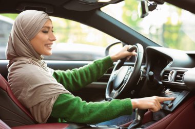 Araba çalma listesi. Türbanlı Arabalı Müslüman Kadın 'ın Yan Görünümü ve Otomatik Ses Sistemi' nde Müzik Dinleme Deneme Sürüşü sırasında Otomobil Seçeneklerini Kontrol Etme, Paneldeki Düğmeye Basma