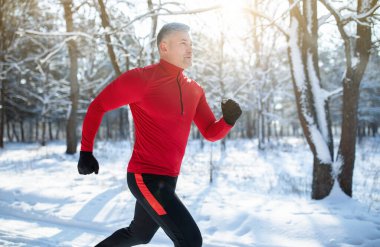 Kış parkında koşan kıdemli atletik adam, fotokopi uzayı. Olgun erkek koşucu dışarıda antrenman yapıyor, doğada koşuyor. Mevsimlik açık hava sporları ve soğuk kanlılık konsepti