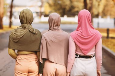 Üç Müslüman bayanın sonbahar günü şehir parkında birlikte yürürken tesettüre girmelerinin arka görüntüsü. Tanımlanamayan İslami Kadın Arkadaşlar Dışarıda Yürüyüşün tadını çıkarıyor. Arapça Biçim ve Moda Konsepti