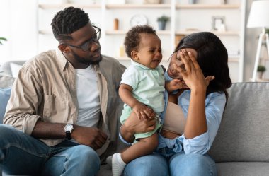 Yorgun siyah annesinin portresi, küçük ağlayan siyah çocuğuyla birlikte evde oturuyor, baş ağrısı ve migren hissediyor, alnına elle dokunuyor, üzgün babası onu rahatlatıyor. Yorgunluk ve Ebeveynlik