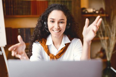 Sanal Web Konferansı. Gülümseyen genç bayan yöneticinin portresi dizüstü bilgisayarla çevrimiçi video görüşmesi yapıyor, kamera ve danışman müşteriyle konuşuyor, masada oturuyor,