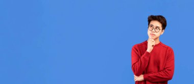 İyi teklif. Gözlüklü dalgın Asyalı adamın portresi fotokopi odasına bakıyor, çenesine dokunuyor, mavi stüdyo arka planında soyutlanıyor. Düşünceli genç adam düşünüyor ve karar veriyor.