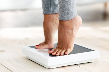 Evde terazinin üzerinde duran, ağırlığını ölçen, ayaklarına yakın duran genç siyahi kadın görüntüsü. Tanımlanamayan Afrikalı Amerikalı kadın zayıflama diyetinin sonucunu kontrol ediyor.