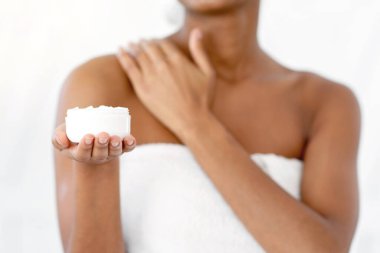 Rahatla, boş zaman, nemlendirici ve yaşlanmayı önleyici cilt bakımı. Binlerce yıllık gülümseyen Afro-Amerikan kadın blogcu duş aldıktan sonra vücuda krem sürerek kavanoza boş alan öneriyor ve sunuyor