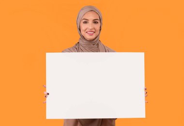 Sarı Stüdyo Arkaplanı Üzerine Metin Reklamları için Boş Poster Tahtası Tutan Müslüman Kadın Başörtüsü Giyiyor. İslami Kadın Boş Kağıt Sancak İlan Veriyor. Model