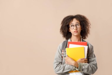 Üzüntü ve yorgunluğun doğal insani duyguları. Gözlüklü, sırt çantalı, not defterli, sarı arka planda, stüdyo çekimlerinde izole edilmiş, boş yere bakan yorgun Afrikalı Amerikalı öğrenci.