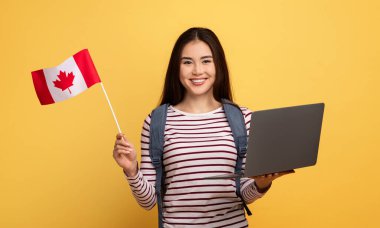 Asyalı genç bir kadın gururla bir elinde Kanada bayrağı, diğer elinde dizüstü bilgisayar, parlak sarı bir arka plana karşı gülümsüyor, Kanada Günü için coşkusunu sergiliyor.