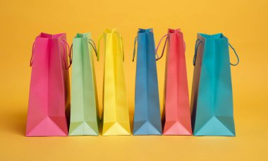 Pembe, yeşil, sarı ve mavi olmak üzere çeşitli renklerde sergilenen altı adet kağıt alışveriş torbası bir sırada duruyor..