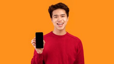 Bu uygulamayı tavsiye ediyorum. Elinde siyah boş ekranla akıllı telefonu tutan gülümseyen Asyalı adam kameraya gösteriyor. Model için boş alanı olan Gadget, turuncu stüdyo arka planında izole edilmiş.