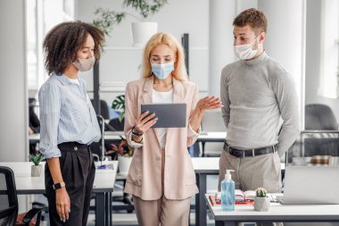 İş sırasında müdüre sorulan sorular. Koruyucu maskeli kadın patron tablet 'e bakar ve birlikte çalıştığı ofisteki, panoramadaki, serbest alandaki erkek ve Afrikalı Amerikalı kadının görevlerini kontrol eder.