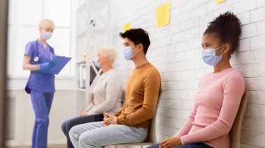 Coronavirus Aşılama Konsepti. Covid-19 aşısını bekleyen siyahi kız hastane bekleme odasında çeşitli insanlarla kuyrukta bekliyor. Covid 19 Virüs Önleme ve Tıbbi Tedavi Konsepti