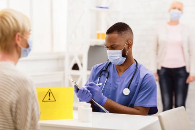 Covid-19 Aşı Konsepti. Coronavirus aşısı aşısından önce hastane odasında oturan kadın hastayla konuşan Afrikalı bir doktor. Kapsamlı Bağışıklık Sistemi Tıbbi Kampanyası