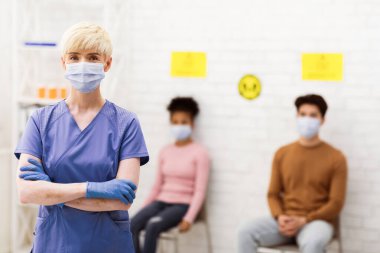 Coronavirus hastalarının önünde dikilen maskeli kadın hasta hastalar bekleme odasında kameraya bakıyor. Profesyonel Klinik Personeli, Doktor ve Hemşire Mesleği. Boşluğu Kopyala