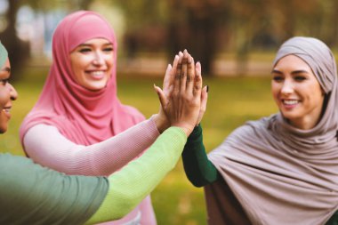 Üç mutlu modern Müslüman kadın tesettüre girmiş dışarıda park yerinde ayakta beşlik çakıyor. Arap Kadın Birliği ve Birlikteliği, Kadın Arkadaşlığı Konsepti. Ellere Seçici Odaklanma
