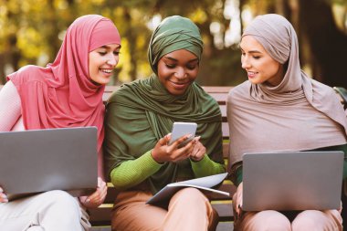 Eğitici Mobil Uygulama. Müslüman Öğrenci Bayanlar Arkadaşlarının Akıllı Telefonuna Bakıyor, Dışarıda oturan bilgisayarları ve telefonları kullanarak Birleştirip Öğreniyorlar.