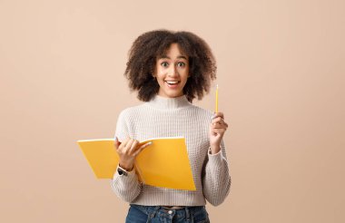 Çalışma fikri ve karantina sonrası dersler. Bin yıllık mutlu Afro-Amerikan kadını elinde not defterini tutuyor ve kalem kaldırıyor, sarı arka planda izole edilmiş, fotokopi alanı, stüdyo çekimi, kesilmiş.