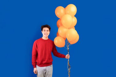 Kutlama ve Parti Konsepti. Elinde sarı balonlar tutan mutlu Asyalı adam portresi, stüdyoda duruyor, mavi arka planda izole edilmiş, afiş. Gülümseyen adam etkinliğe hazır.