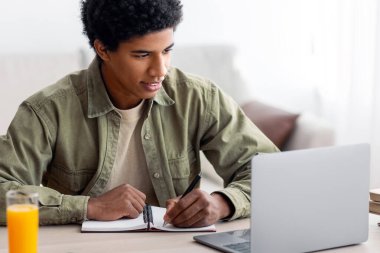 Evde eğitim kavramı. İnternetteki konferans sırasında ya da evde internet dersinde siyahi öğrenci kitabı yazıyor. Afrikalı Amerikalı gençler eğitim kursuna gidiyor, webinar 'a katılıyorlar.