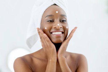 Cilt bakımı, güzellik dersleri ve cilt bakımı. Genç ve çekici Afrikalı Amerikalı kadın sabahları cilt için nemlendirici krem kullanıyor ve aynaya bakıyor, boş alan.