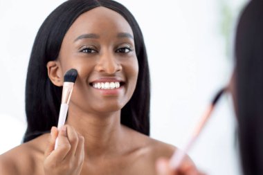 Kadın işe gitmek için hazırlanıyor, sabah rutin çıplak makyaj yapıyor, evdeki banyoya allık sürüyor. Mutlu Afro-Amerikan milenyum bayanı havluyla aynaya bakıyor.