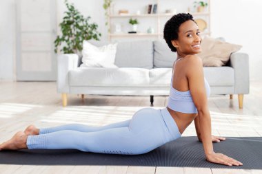 Evdeki spor minderinde yoga yapan, kobra pozu veren zinde bir zenci kadın. Pozitif Afrikalı Amerikalı kadın ev içi eğitim alıyor, esneklik egzersizleri yapıyor, panorama
