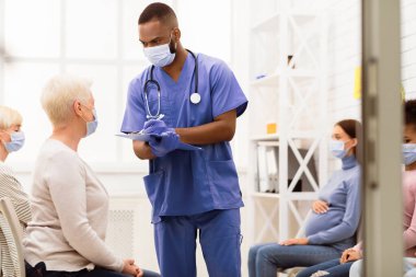 Erkek hemşire, Kıdemli Hasta Kadın 'la Doktor randevusundan önceki 19 semptomu konuşuyor. Hastanede kuyrukta oturuyor, maske takıyor. Coronavirus, Kapalı Tıbbi Tedavi Konsepti