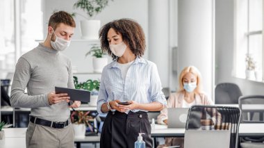 İş ve koronavirüs salgınına karşı koruma fikirleri. Müdürün dediğine göre koruyucu maske tabletindeki Afro-Amerikan kadın iş yerine yakın bir yerde dizüstü bilgisayar ve bir şişe antiseptik kullanıyor.