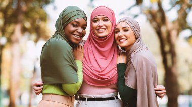 Üç Müslüman kadın tesettüre poz veriyor. Şehir parkında kameraya gülümsüyor. Modern İslami Kadın Grup Portresi, Arkadaşlık ve Birliktelik. Panorama