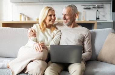 Mutlu bir çift kanepede oturur, rahat oturma odalarında dizüstü bilgisayar kullanırken birbirlerine gülümserler, boş zamanlarında bağ kurar ve keyif alırlar..