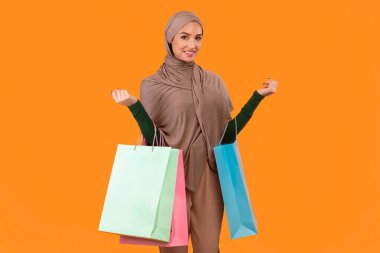 Başarılı bir alışveriş. Sarı Stüdyo Arkaplanının Üzerinde Duran Bir Çok Alışveriş Çantası Tutan Mutlu Arap Müslüman Kadın. Arap Kadın Moda ve Kıyafeti Konsepti