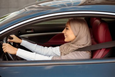Mutlu Araba Sahibi. Yeni lüks araba kullanan, başörtüsü takan mutlu Arap kadının yan görünüm portresi. Kuaförde oturan, direksiyonda oturan neşeli Müslüman kadın.