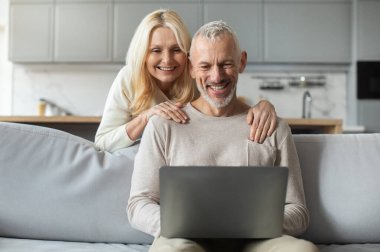 Neşeli bir son sınıf çifti rahat bir kanepede oturur ve dizüstü bilgisayarla meşgul olurlar. Kadın gülümser ve erkeğin omuzlarına yaslanır. Davetkar yaşam alanlarında sıcak bir atmosfer yaratır..