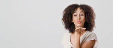 Mutluluk, gülümseme ve kendini izole etme konusunda olumlu duygular. Şirin kıvırcık saçlı Afrikalı Amerikalı kadın kameraya üfleme öpücüğü veriyor, arka planda izole edilmiş, kesilmiş, stüdyo fotoğrafı, kopyalama alanı