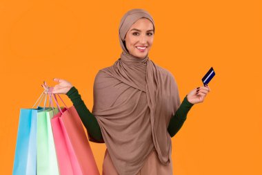 Mutlu Müslüman Kadın Alışveriş Torbası ve Kredi Kartı Alırken Stüdyoda Sarı Arkaplan 'ın üzerinde duruyor. Arap Kadın Moda ve Kıyafeti, Mutlu Alıcı Konsepti