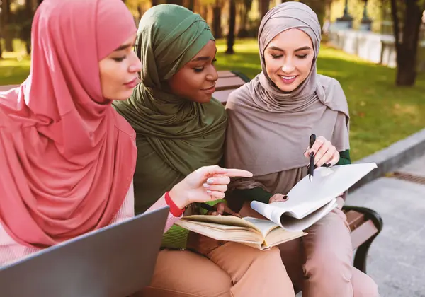 Kampüs parkının dışındaki bankta birlikte oturan üç Müslüman kız öğrenci birlikte öğreniyor. Üniversite Eğitimi, Öğrenim ve Bilgi Konsepti. Seçici Odaklanma