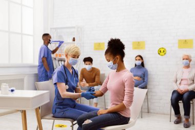 Coronavirus Aşı Kampanyası. Siyahi genç kıza Covid-19 aşısı yapan hemşire çok ırklı hastalar bekleme odasında otururken. Corona Virüs Nüfus Bağışıklığı Kavramı