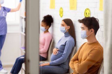 Çok ırklı insanlar, doktor randevusu ve Coronavirus aşısı için bekleme odasında sırada bekleyen tıbbi maskeler takıyorlar. Covid-19 Aşı, Nüfus Bağışıklığı Kampanyası