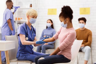 Covid-19 Aşılama. Coronavirus aşısı olan Afrikalı Amerikalı genç kız hastanede doktorla otururken koluna iğne vuruldu. Corona Virüs Tedavisi ve Önleme. Seçici Odaklanma