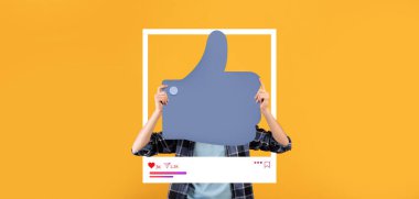 Bir insan, parlak sarı bir arkaplana karşı yüzünün önünde büyük bir işaret tutar. Bu, çevrimiçi bağlanma ve sosyal medya ve blog yazımında olumlu geri bildirimi temsil ediyor.