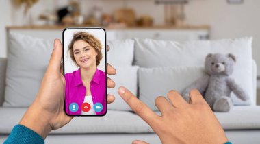 Bir insan evde dinlenirken biriyle görüntülü konuşmak için akıllı telefon kullanır. Oturma odasında rahat bir kanepe ve bir oyuncak ayı var, davetkar bir atmosfer yaratıyor..