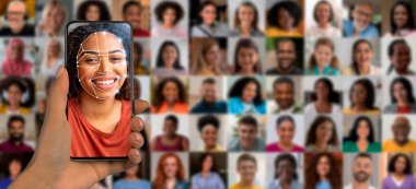 Bir insan, yüzünü taramak için akıllı telefon kullanır. Arka planda çeşitli yüzlerden oluşan bir kolaj yer almakta, modern teknolojinin kişisel kimliklendirmedeki yeteneklerini göstermektedir..